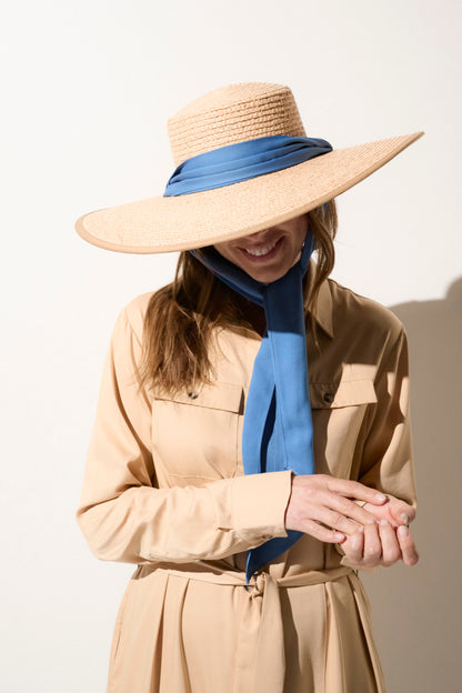 Chapeau anti-UV en paille beige avec ruban bleu, porté par une femme, idéal pour une protection solaire élégante.