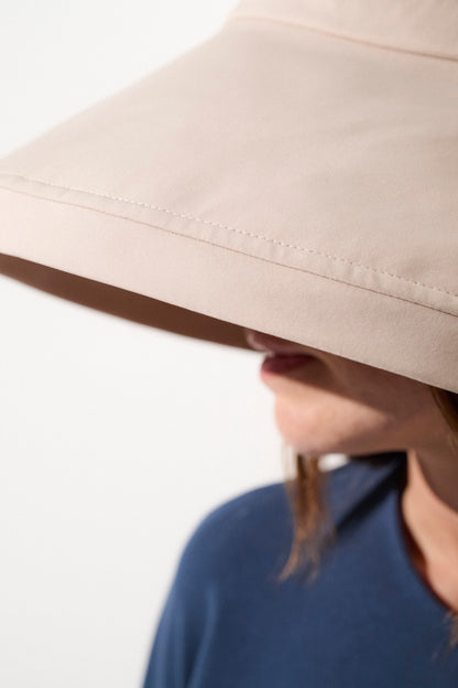 Chapeau anti-UV beige UPF50+ porté par une femme, parfait pour les activités extérieures et la protection solaire.