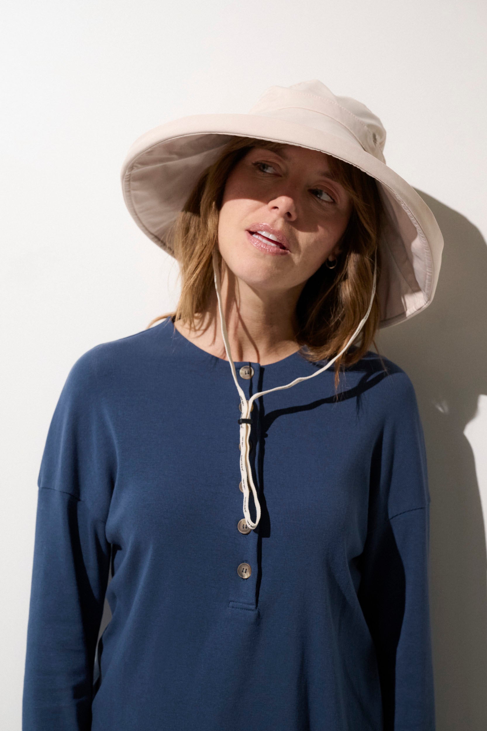 Femme portant un chapeau anti-UV beige UPF 50+ et un haut bleu, idéal pour la protection solaire à l'extérieur.