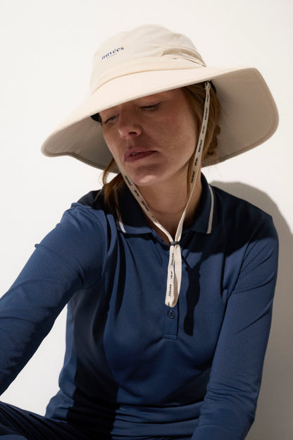 Femme portant un chapeau anti-UV beige, avec polo bleu, idéal pour le golf, offrant protection solaire UPF50+.