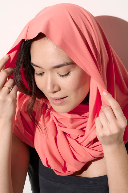 Femme portant un foulard léger anti-UV corail, idéal pour une protection solaire élégante. UPF 50+.