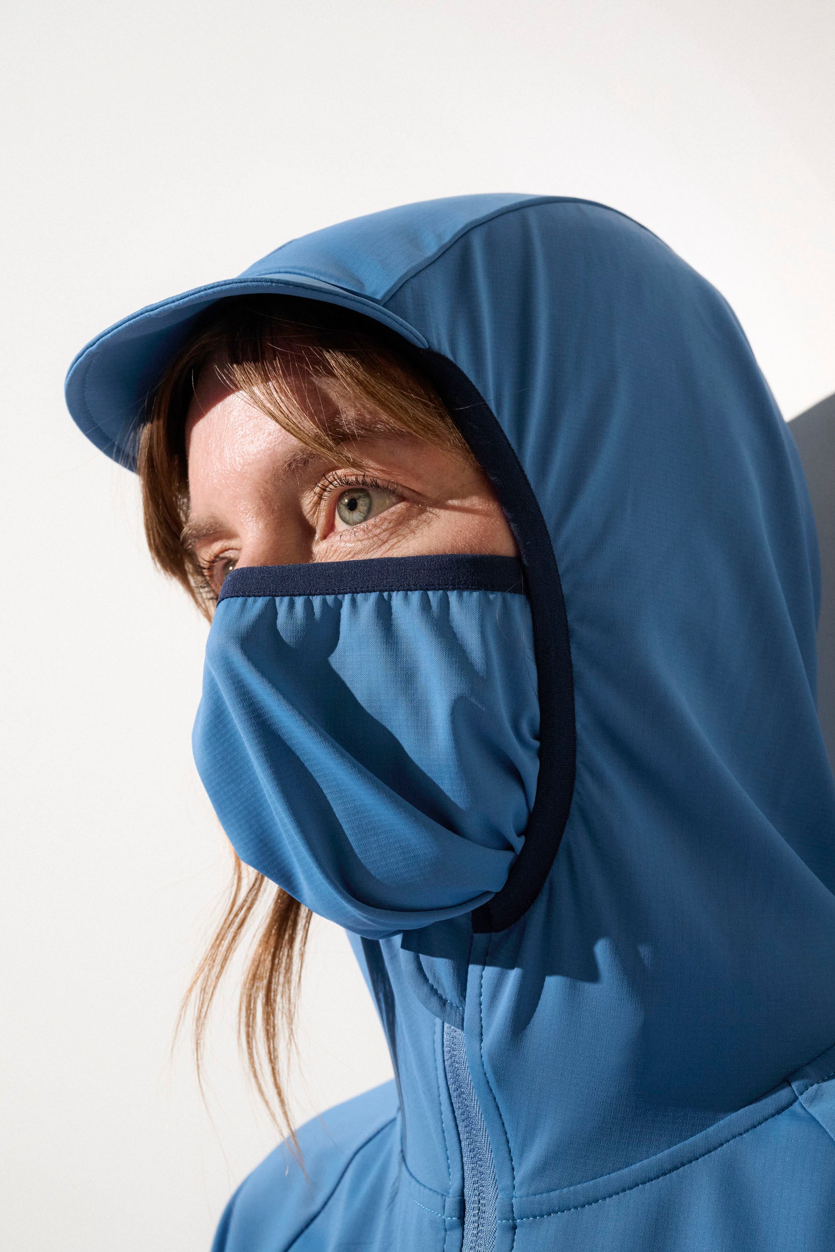 Veste anti-UV femme en bleu, avec capuche et masque intégré, pour une protection solaire UPF50+ lors d'activités extérieures.