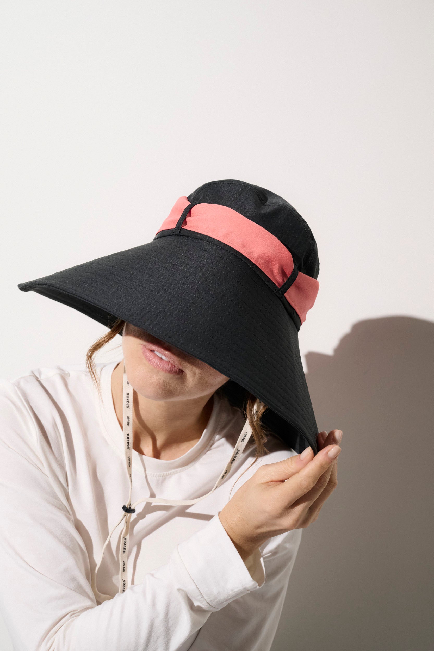 Chapeau anti-UV noir avec bande rose, UPF 50+, porté par une femme pour une protection solaire quotidienne.