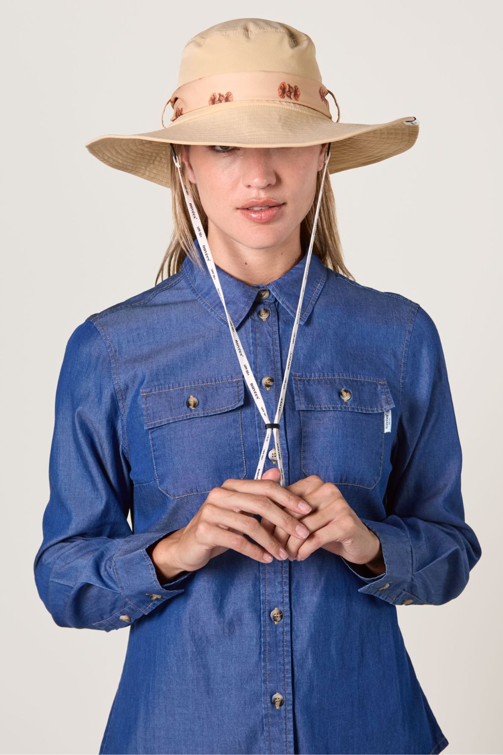 Chapeau anti-UV beige pour femme, protection solaire UPF50+, porté avec chemise en jean, au style décontracté.