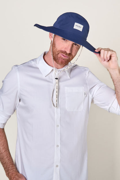 Homme portant un chapeau anti-UV bleu avec chemise blanche, idéal pour la protection solaire en extérieur.