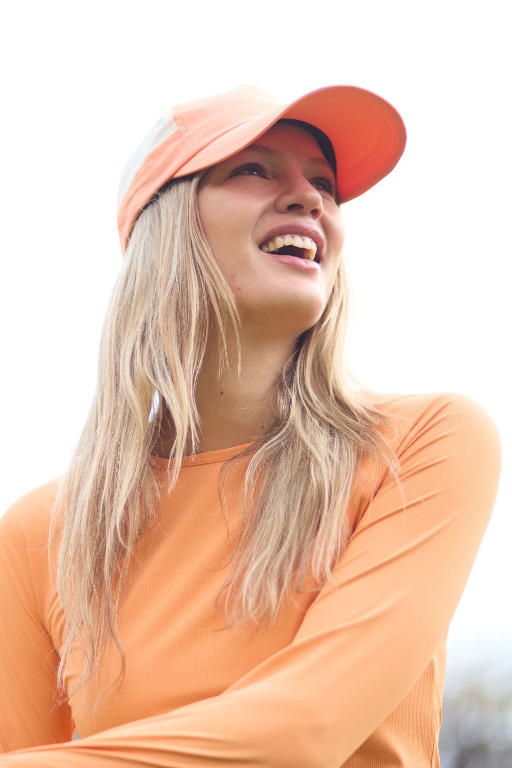 Femme souriante portant une casquette anti-UV orange, idéale pour les activités de plein air.