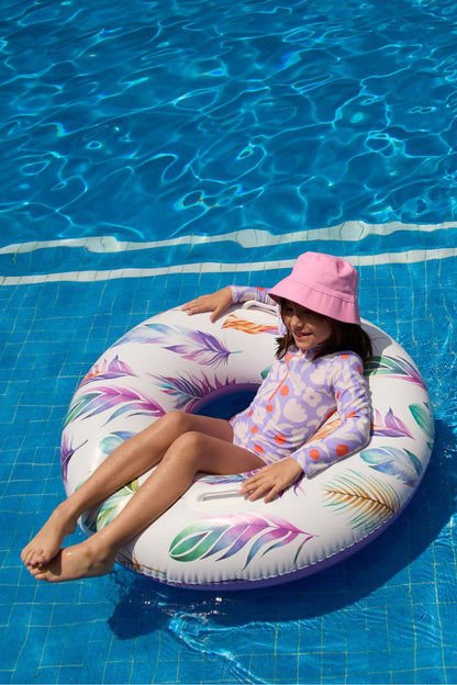 Fille portant un maillot de bain anti-UV à manches longues UPF 50+, flottant sur un anneau dans une piscine.