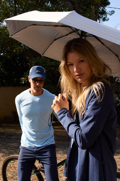 Femme utilisant une ombrelle anti-UV UPF50+ pour se protéger du soleil, accompagnée d'un homme au look décontracté.