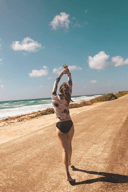 Femme marchant sur la plage en maillot de bain anti-UV noir et haut à manches longues, exposée au soleil.